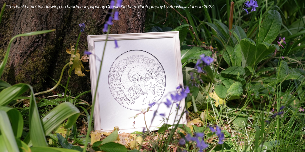 Anastasia Jobson photograph of Charlie Kirkham ink drawing showing a dragon eating a lamb, displayed against a tree in  a wood full of bluebells 
