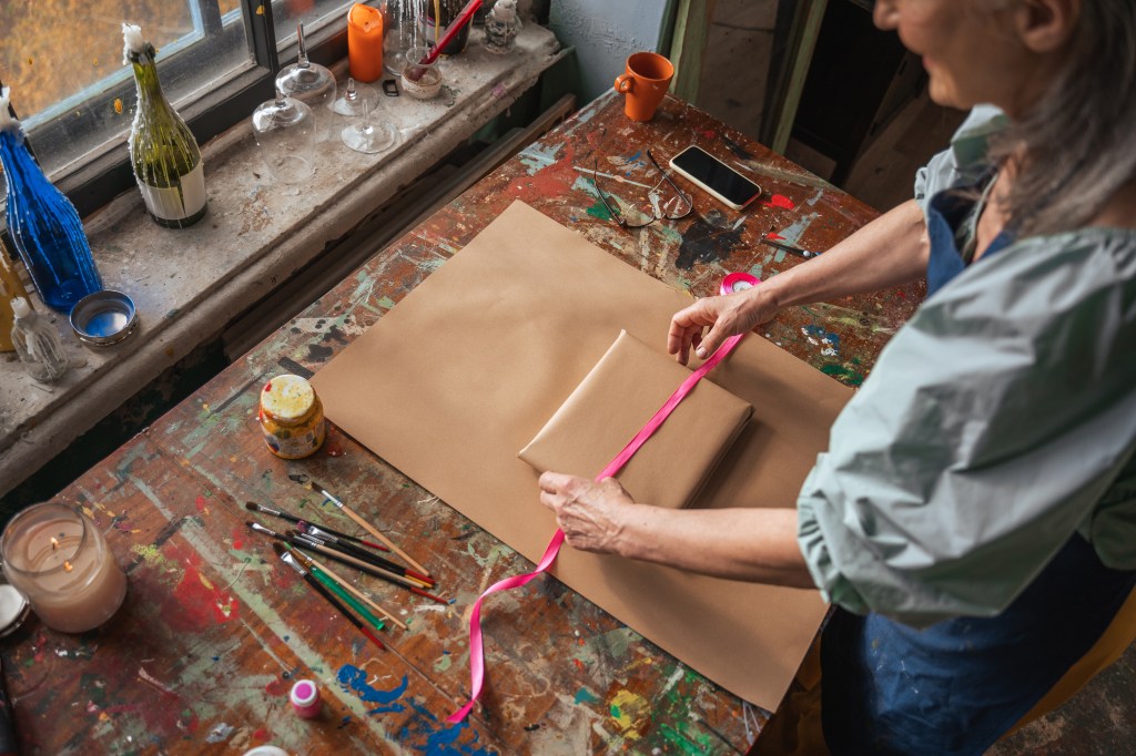 female artist packing artwork to buyer from online art exhibition. brown paper wrapping and pink ribbon