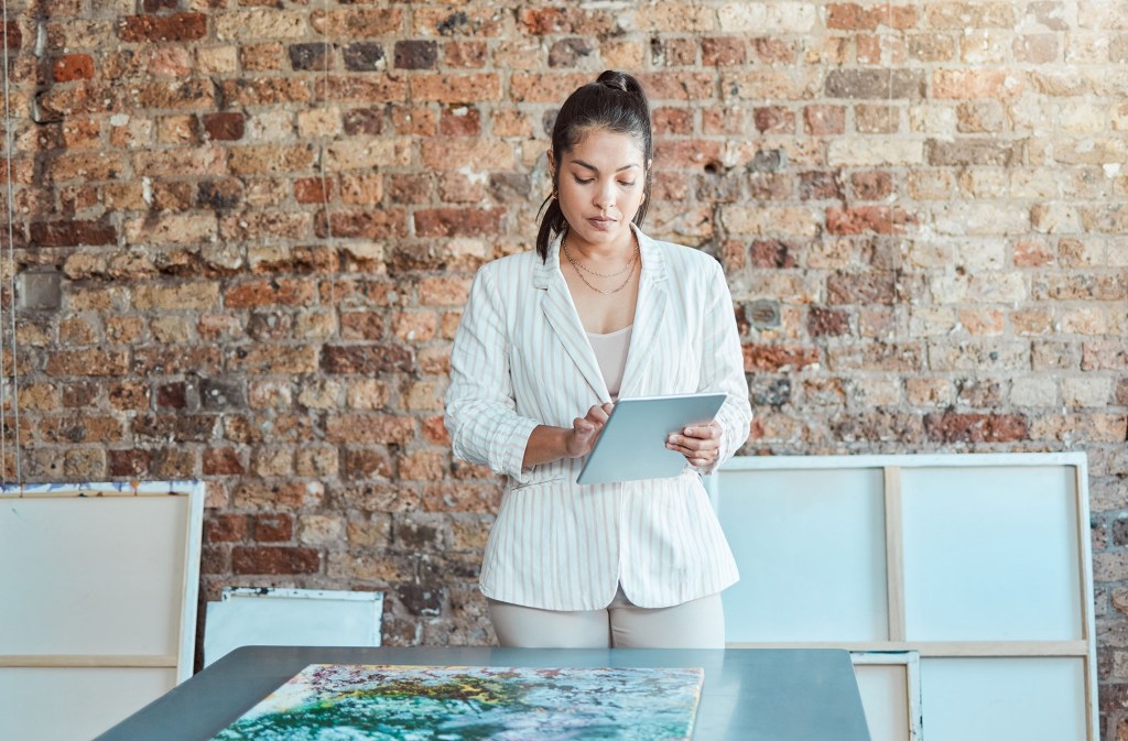 Selecting an online show, young woman with tablet in room of artwork