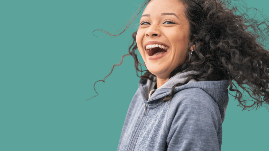 here are 5 signs you're not fulfilling your artistic potential happy laughing woman with flowing curls smiling in blue hoody