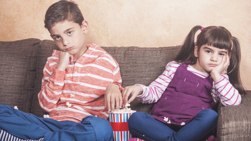 two children boy girl looking bored with popcorn watching a film 