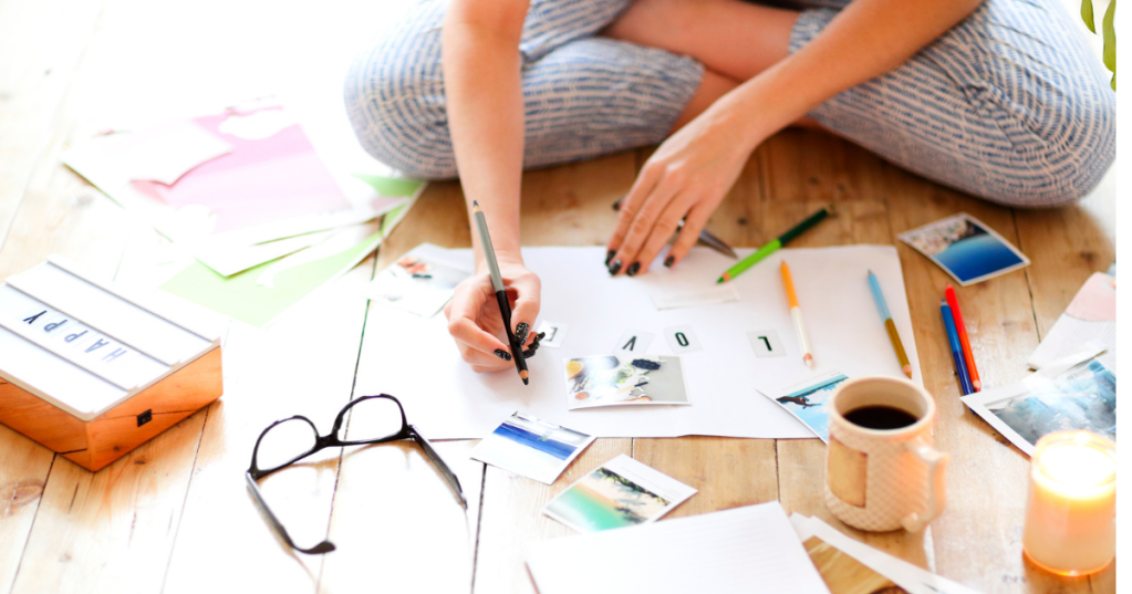 female with white skin and dark nails drawing on floor with coffee and candle