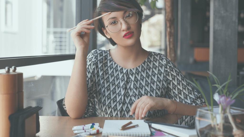 artist thinking about how to budget with pencils and paints in front of her, skyscraper window background

